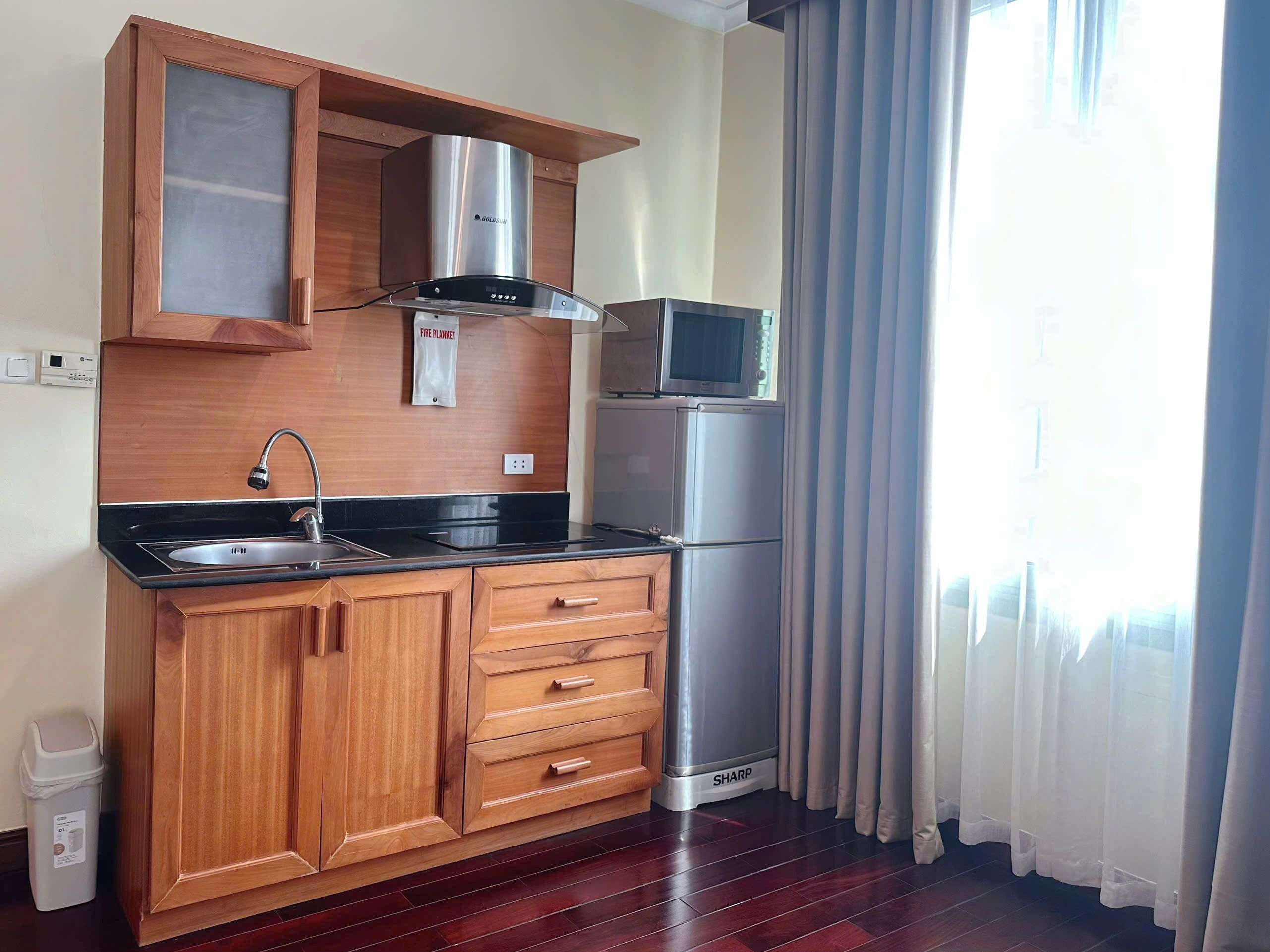 A compact kitchen with wooden cabinets, a stainless steel range hood, a microwave, and a refrigerator.