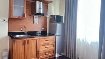 A compact kitchen with wooden cabinets, a stainless steel range hood, a microwave, and a refrigerator.