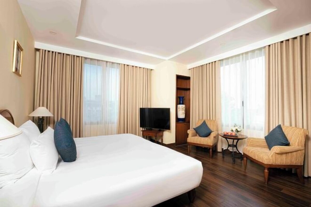 A hotel room with a large bed, two armchairs, a small table, a TV, and curtains.