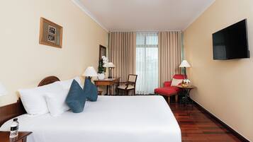 Quarto de hotel com cama grande, escrivaninha, cadeira, televisão e janela com cortinas.