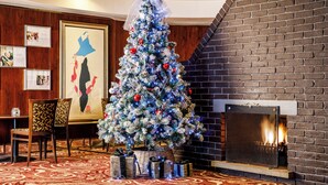 Un árbol de Navidad adornado con adornos y luces, una chimenea, cuadros enmarcados y una alfombra estampada.