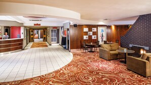 Et hotel lobby med reception, buet tæppe, siddeområde og pejs.