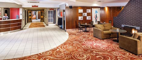 Un vestíbulo de hotel con mostrador de recepción, alfombra ondulada, área de descanso y chimenea.