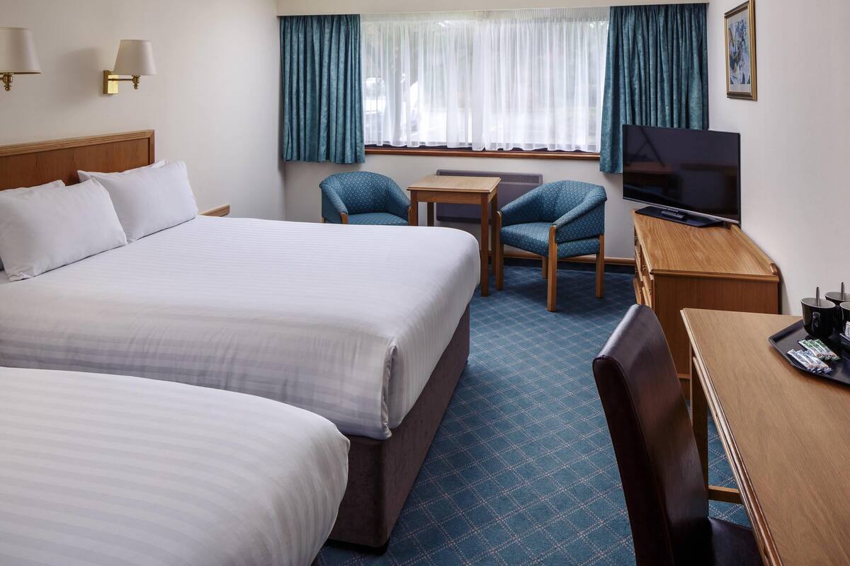 A hotel room with a large bed, a desk, a chair, a television, and a window with curtains.
