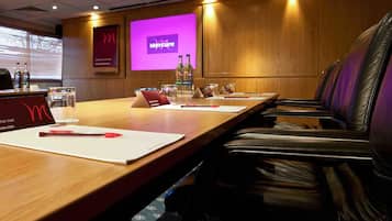 Une salle de conférence avec une longue table, des fauteuils en cuir, un écran de projection affichant le mot « Mercure » et un mur en bois.