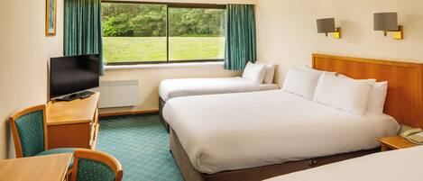 A hotel room with two beds, a desk with a television, and a view of the outdoors.