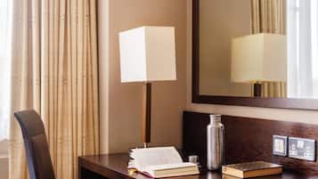 A hotel desk with a lamp, a book, a water bottle, and a mirror.