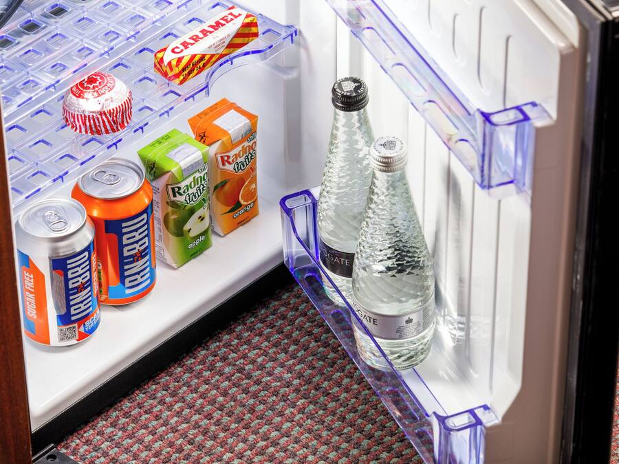 A refrigerator with a crisper drawer, a bottle of water, and various beverages including cans and juice cartons.