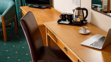 A hotel room with a wooden desk, a laptop, a coffee maker, and a tray with coffee cups and milk packets.