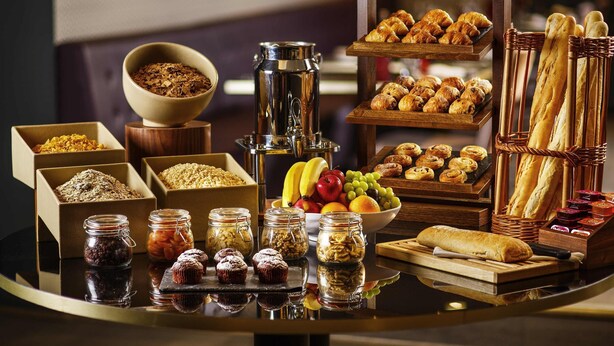 Una mesa de buffet con diferentes opciones de comida, como pasteles, pan y frutas.