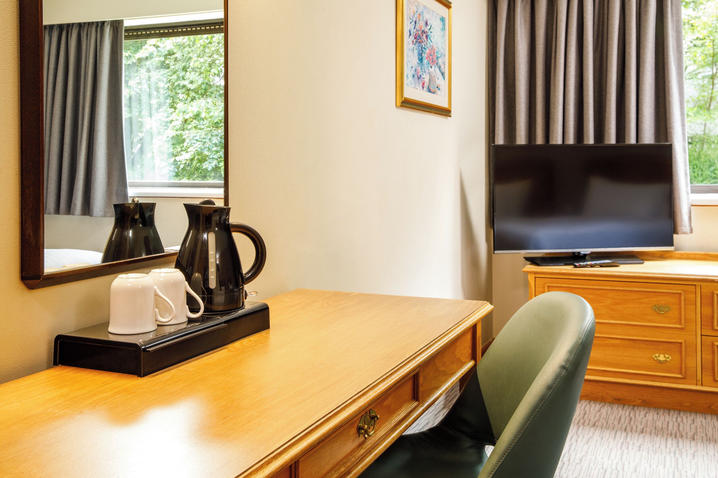 A hotel room with a wooden desk, a television, a coffee maker, and a chair.