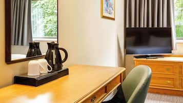 A hotel room with a wooden desk, a television, a coffee maker, and a chair.