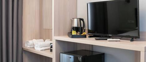 A modern hotel room with a flat-screen TV, a coffee maker, and neatly folded towels on a wooden shelf.