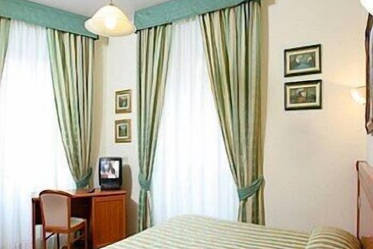 A bedroom with a bed, a desk with a chair, and two framed pictures on the wall.