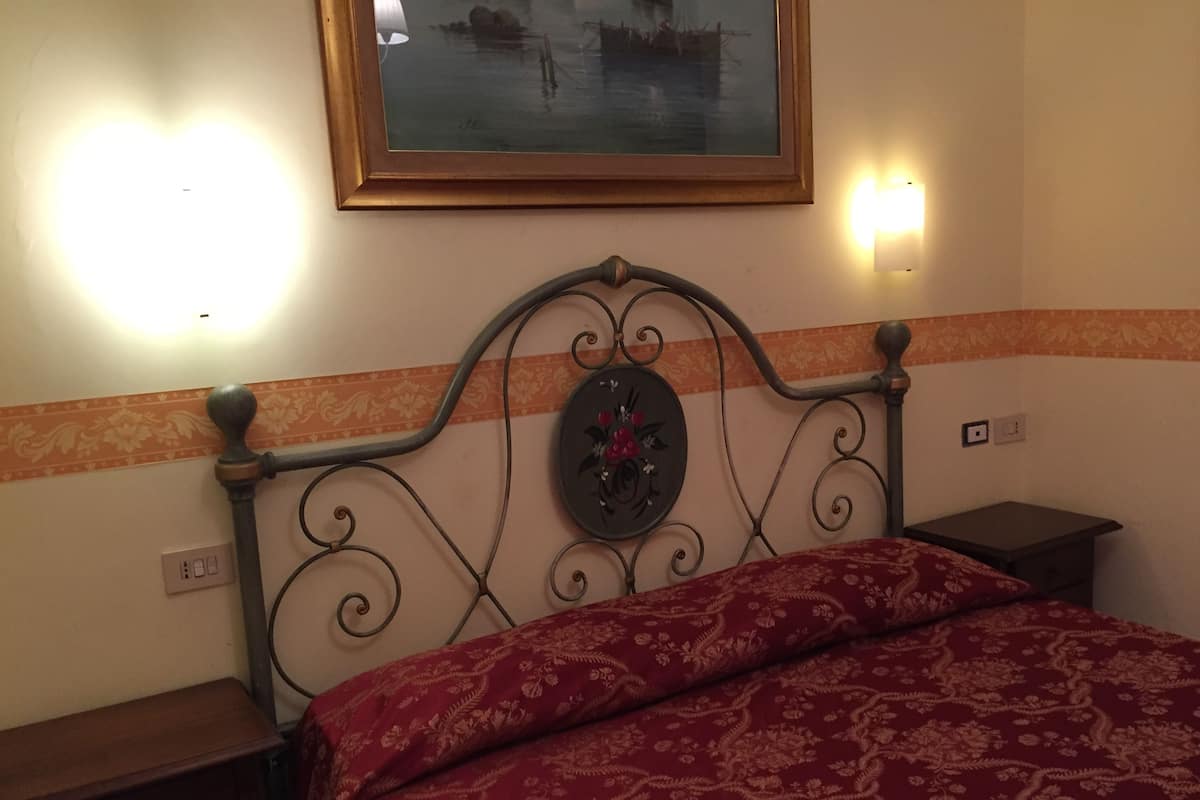 A bed with a floral headboard, a nightstand, a wall-mounted lamp, and a framed picture above the bed.
