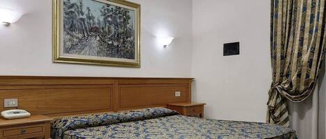 A hotel room with a wooden headboard, a bed with a patterned bedspread, a bedside table with a telephone, and a wall-mounted painting.