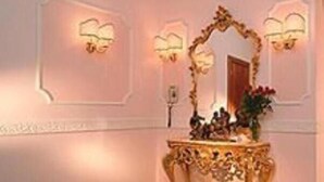 Un passadís amb aplics de paret ornamentals, una petita taula de consola decorativa i un disseny de sòl amb patrons.