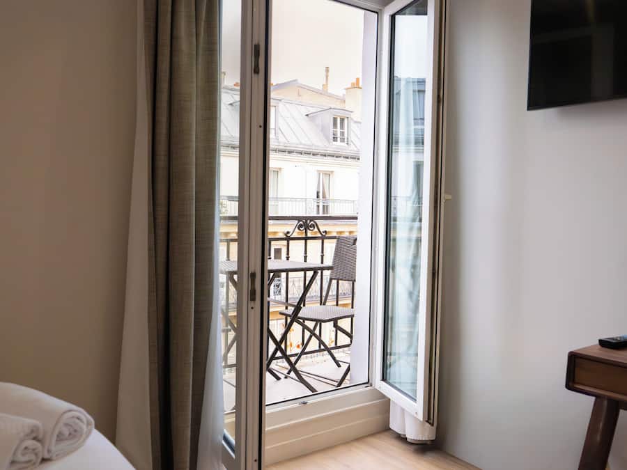 Una habitación de hotel con puerta corrediza de vidrio que da a un balcón exterior con mesa y sillas.