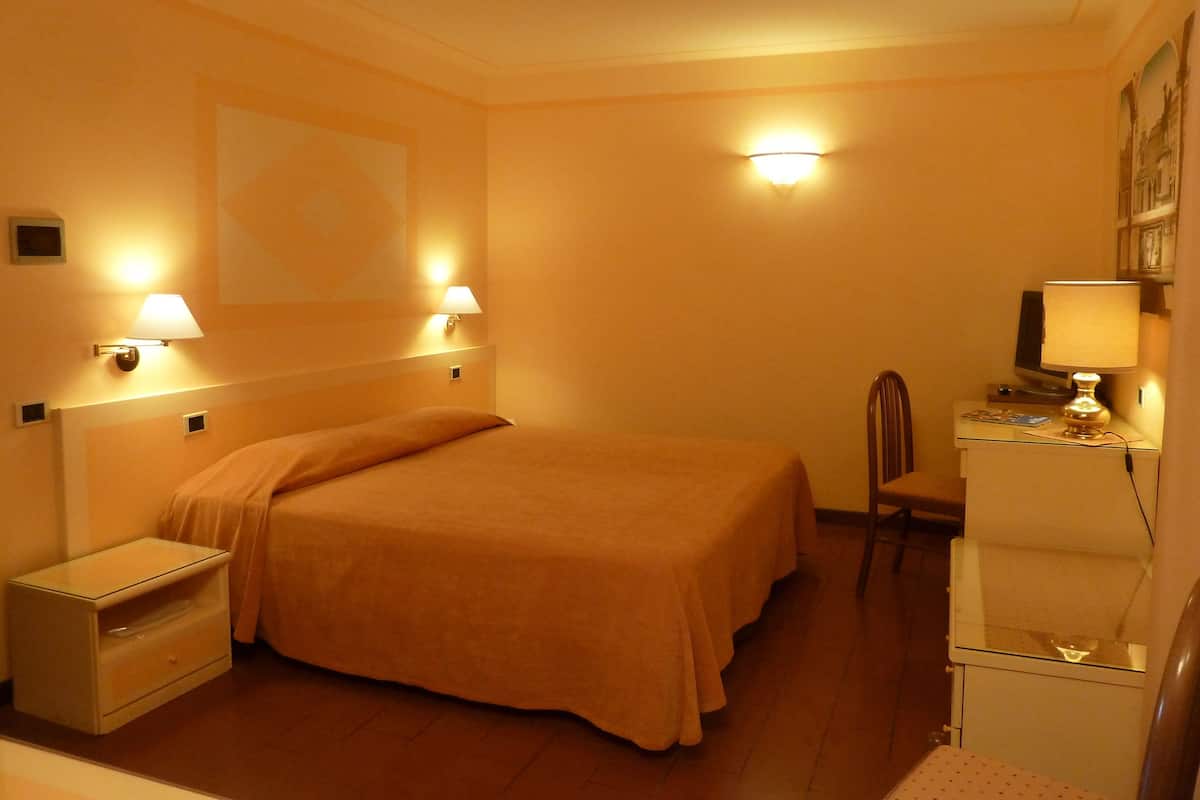 A hotel room with a bed, bedside tables, a desk with a lamp, and a chair.