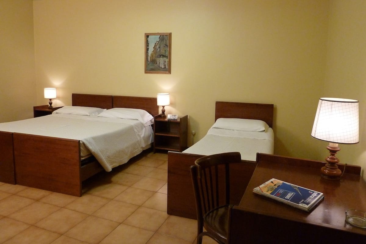 A hotel room with two beds, a desk, a chair, and a table lamp.