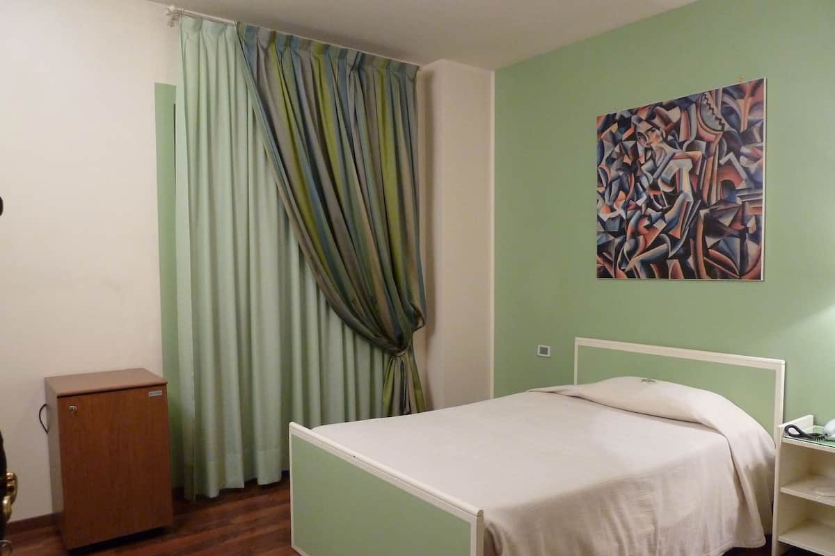 A room with a bed, a small cabinet, and a painting on the wall.