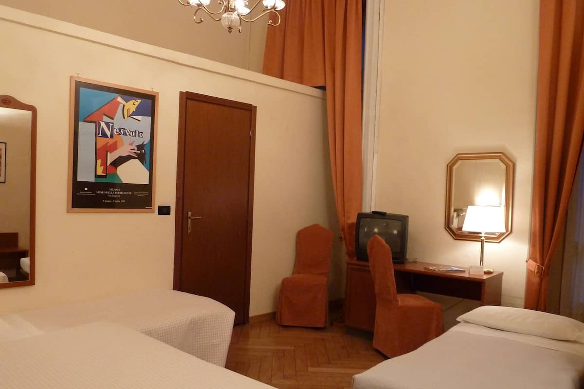 A hotel room with two beds, a television, a desk with a lamp, a chair, and a poster on the wall.