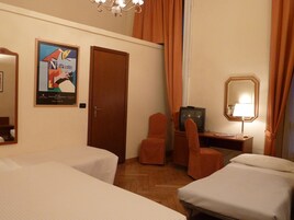 Una camera d'hotel con due letti, una televisione, una scrivania con una lampada, una sedia e un quadro appeso al muro.