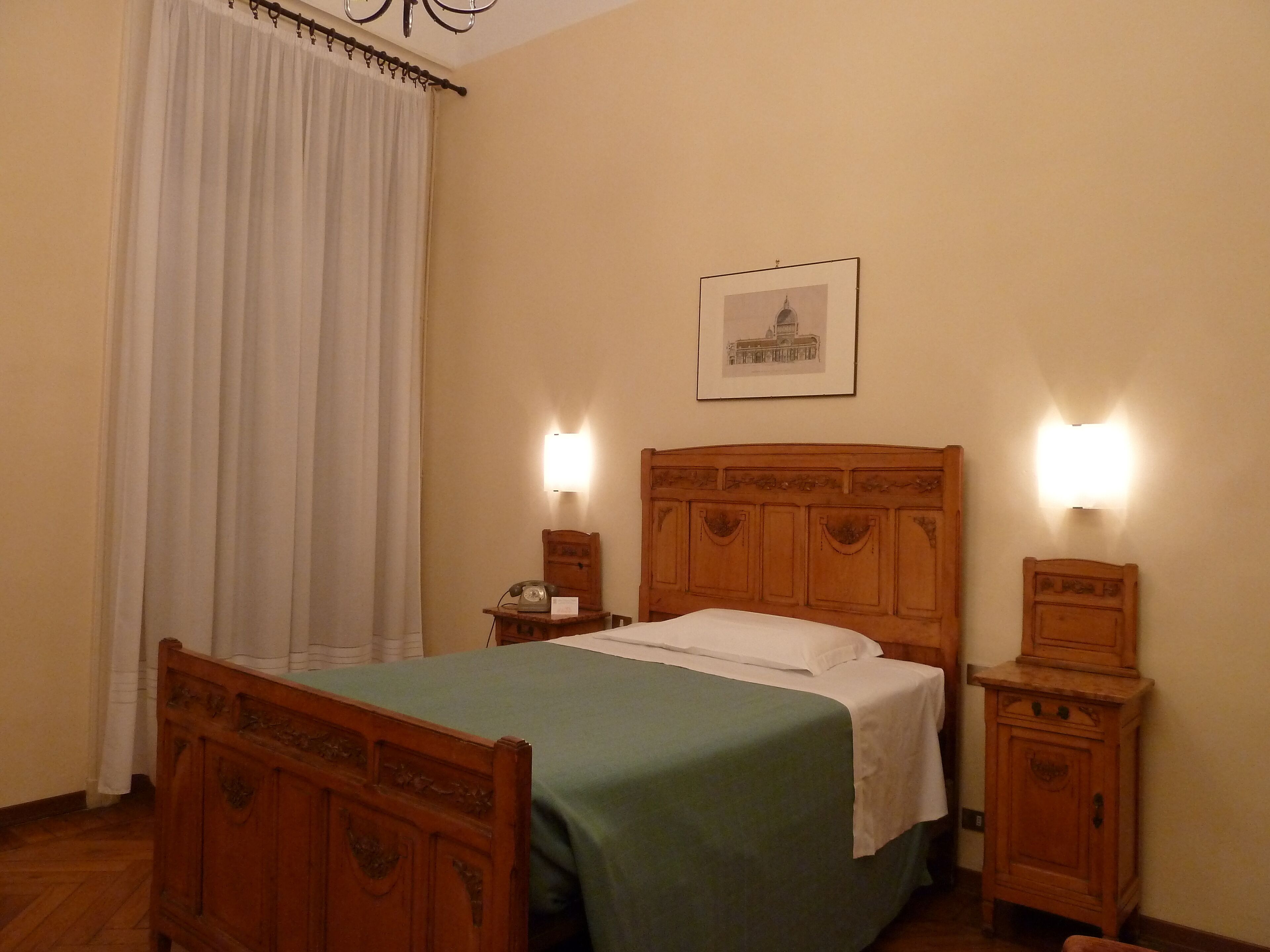 A bedroom with a wooden bed, a nightstand with a telephone, and a wall-mounted light.
