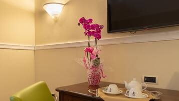 Ein Hotelzimmer mit einem grünen Sessel, einem Schreibtisch mit einer Vase mit rosa Orchideen, einem Fernseher und einer Kaffeestation.