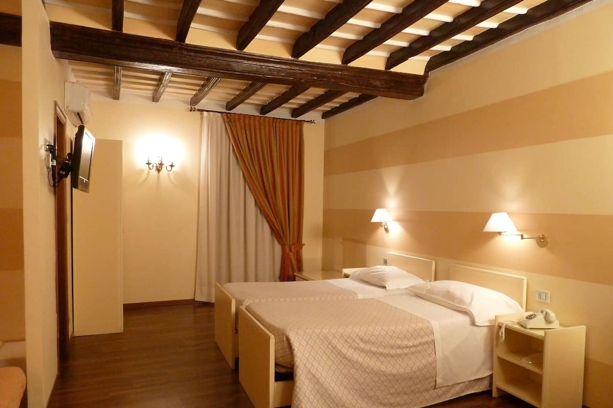 A hotel room with two beds, wooden flooring, a ceiling with exposed beams, and bedside lamps.