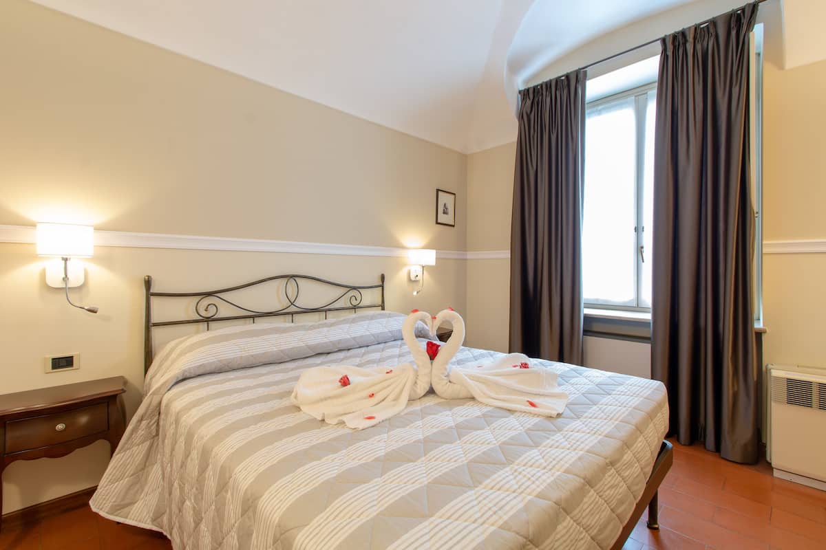 A neatly made bed with a striped bedspread, two wall-mounted lights, a picture on the wall, and a window with curtains.