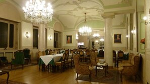 Ein formeller Speisesaal mit Kronleuchtern, grünen, gepolsterten Stühlen und gedeckten Tischen.