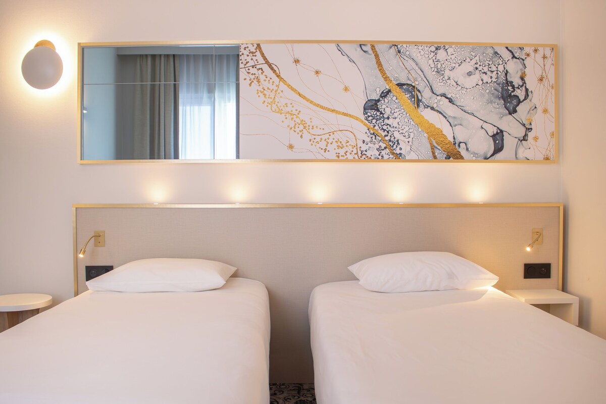 A hotel room with two beds, a large mirror, and a wall art piece.