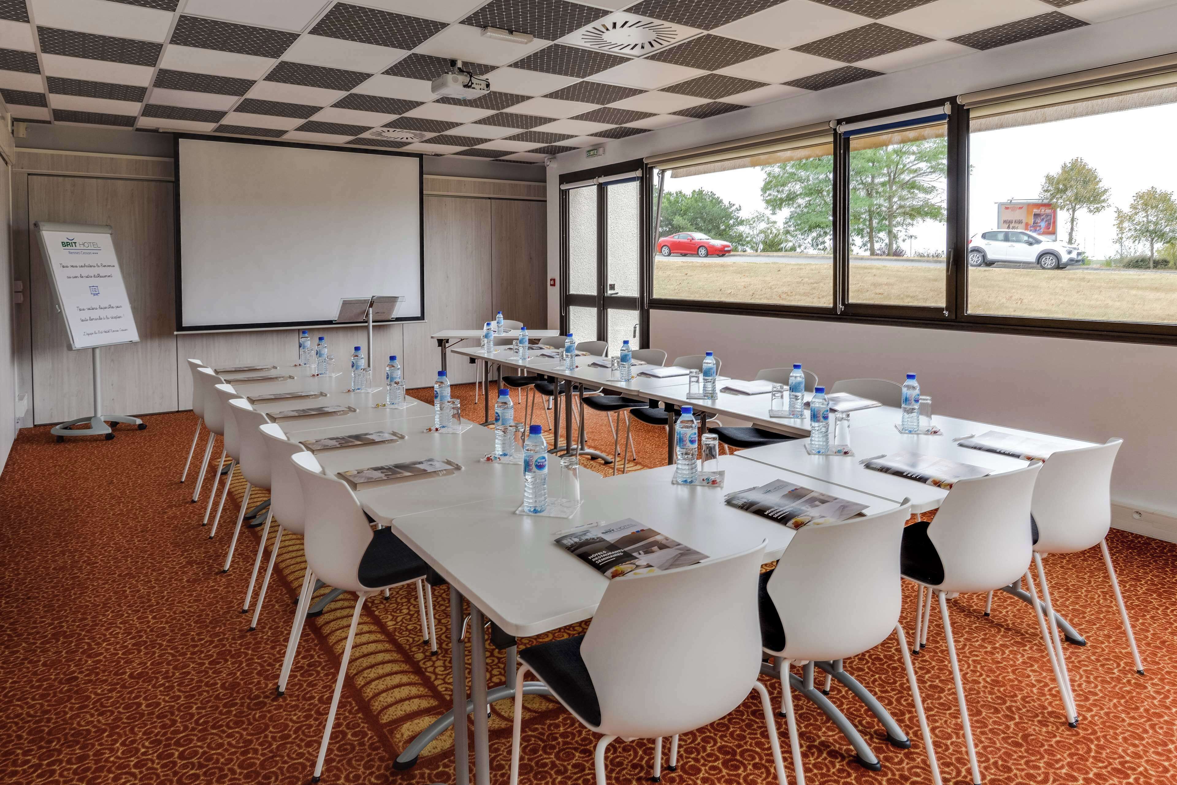 A conference room with a long table, white chairs, water bottles, and a projector screen.