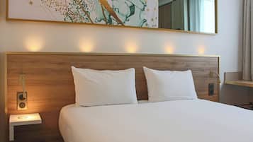 Une chambre d’hôtel avec un grand lit, deux tables de chevet, une lampe fixée au mur et un grand tableau abstrait au-dessus du lit.