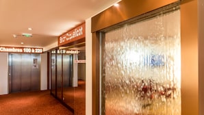 Un pasillo interior con puertas de ascensor que indican “Chambres 100 à 220” y una pared de vidrio esmerilado.