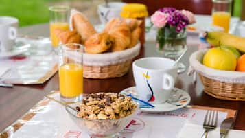 Una mesa de desayuno con cruasanes, un tazón de cereal, una taza de café y un vaso de jugo de naranja.