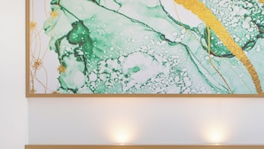 A modern hotel room with a wooden headboard, a bedside table, a wall-mounted speaker, and a large abstract painting above the bed. - Brit Hotel Rennes Cesson - Le Floréal (Cesson-Sevigne)
