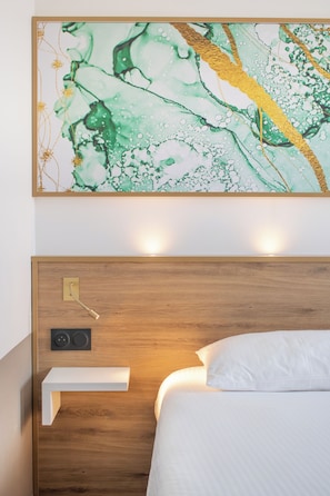 Ein modernes Hotelzimmer mit einem Holzkopfteil, einem Nachttisch, einem an der Wand montierten Lautsprecher und einem großen abstrakten Gemälde über dem Bett.