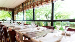 Un restaurante con mesas preparadas para comer, ventanas amplias y vistas al verdor exterior.