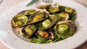 A plate of cooked shellfish with a green sauce, served on a white plate with a fork and knife. - Brit Hotel Rennes Cesson - Le Floréal (Cesson-Sevigne)
