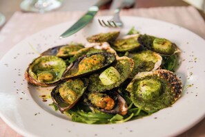 A plate of cooked shellfish with a green sauce, served on a white plate with a fork and knife. - Brit Hotel Rennes Cesson - Le Floréal (Cesson-Sevigne)