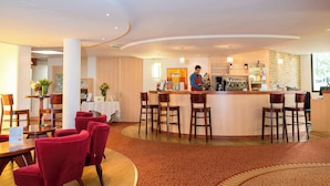 Un vestíbulo de hotel con un mostrador de recepción curvo, sillas tapizadas en rojo y una alfombra estampada.