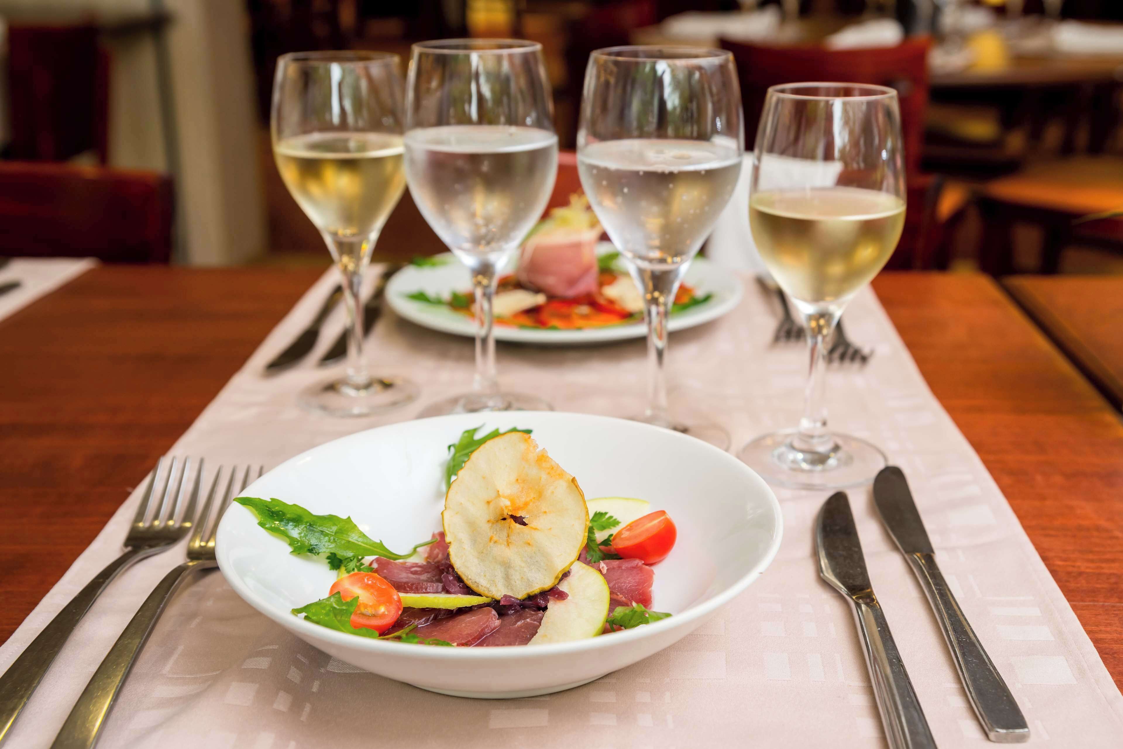 Una mesa de comedor con un plato de comida, un tenedor, un cuchillo y tres copas de vino.