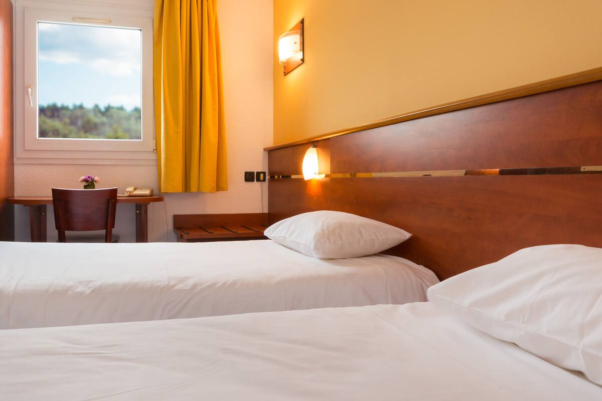 A hotel room with two beds, a desk, and a window with curtains.