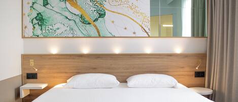 Habitación de hotel con una cama grande, cabecera de madera, mesitas de noche, un espejo montado en la pared y un cuadro abstracto de gran tamaño.