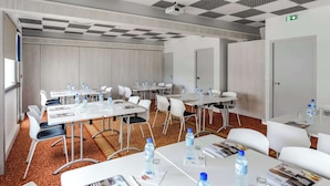 A conference room with white tables, chairs, and water bottles. There are doors and a projector on the ceiling. - Brit Hotel Rennes Cesson - Le Floréal (Cesson-Sevigne)