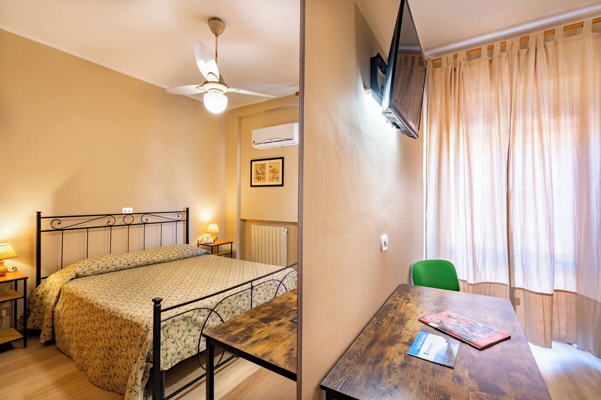 Une chambre à coucher comprenant un lit, une table de chevet, une lampe et un téléviseur fixé au mur.