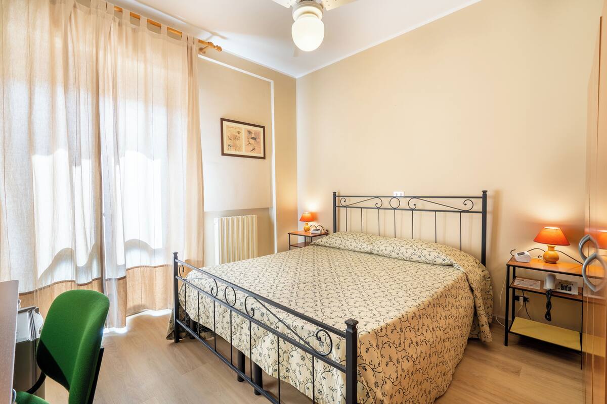 Une chambre à coucher bien rangée, avec un lit, des tables de chevet, une chaise et un radiateur.