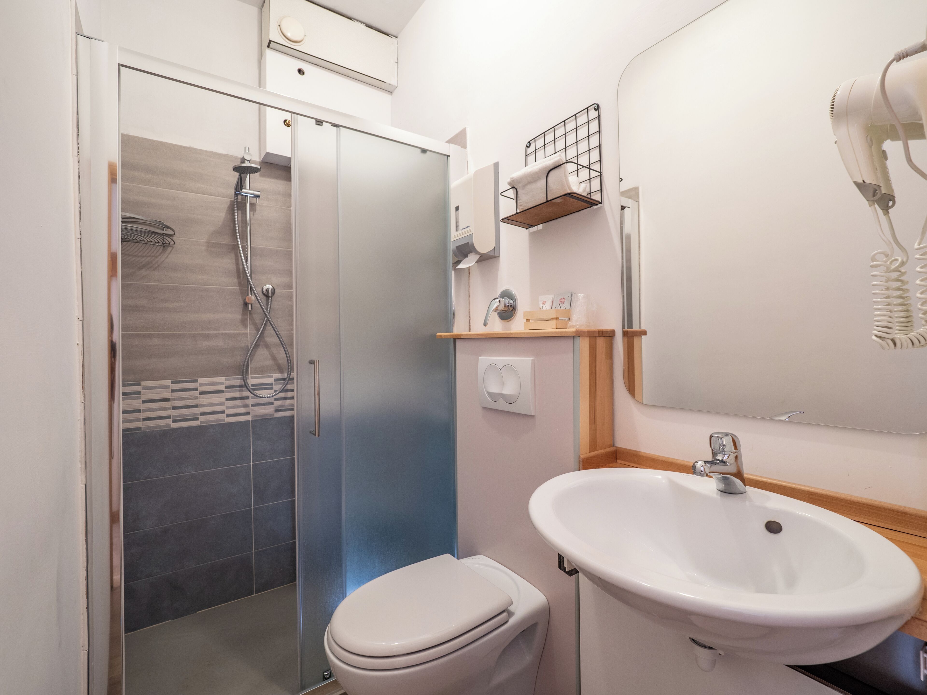 Un baño moderno con cabina de ducha de vidrio, inodoro blanco y lavabo con espejo superior.